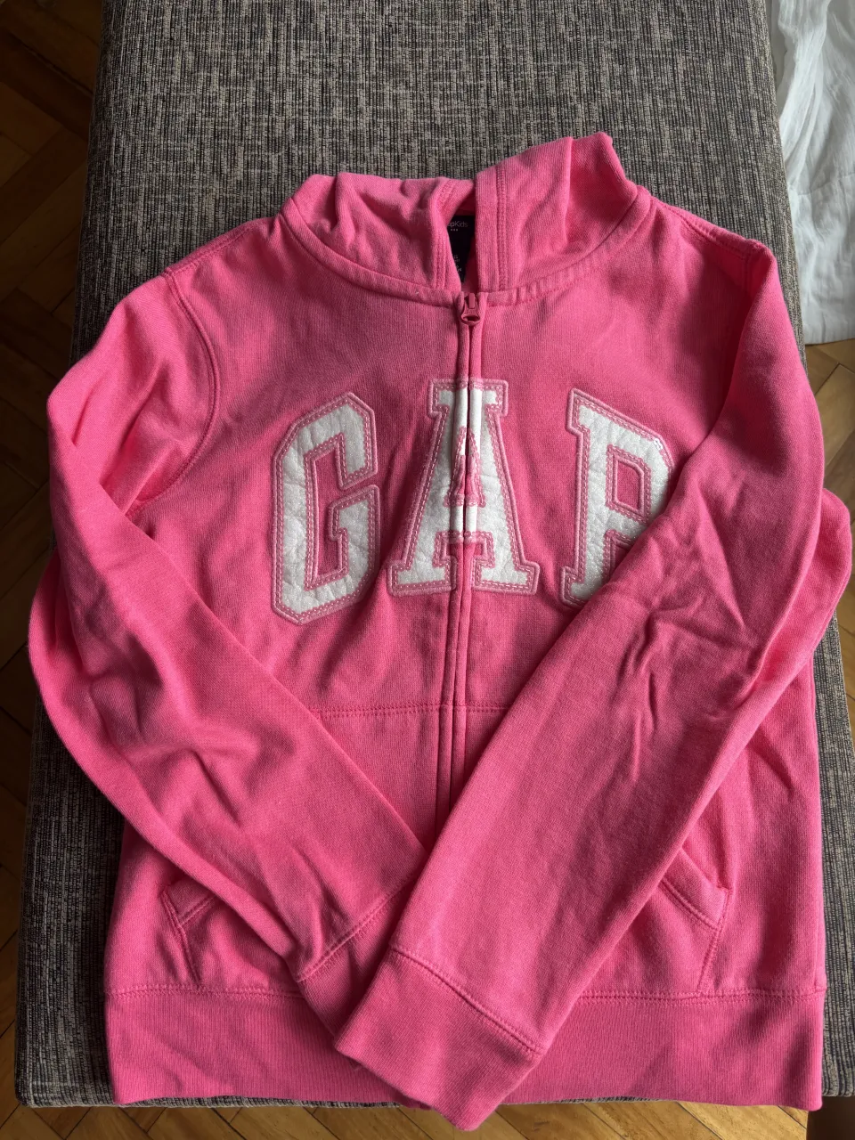 Buzo rosa con cierre y capucha, tiene el logo de GAP bordado en blanco en el frente. Ideal para un look casual y cómodo.