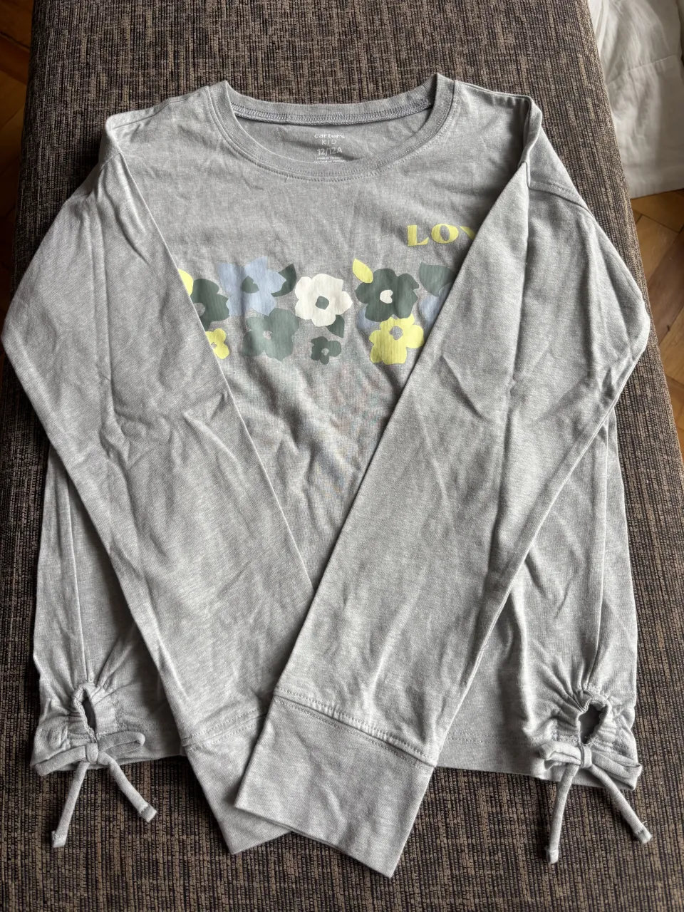 Remera gris de manga larga con estampa de flores y la palabra "LOVE" en amarillo. Tiene detalles de lazo en los puños.