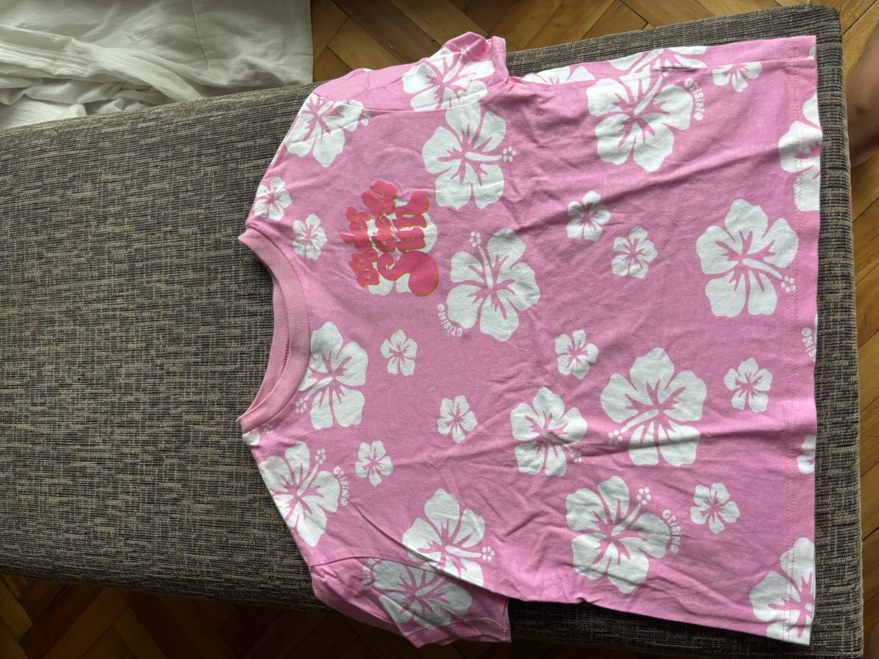 Remera rosa estampada con flores blancas y un diseño en el frente. Ideal para un look casual y fresco.