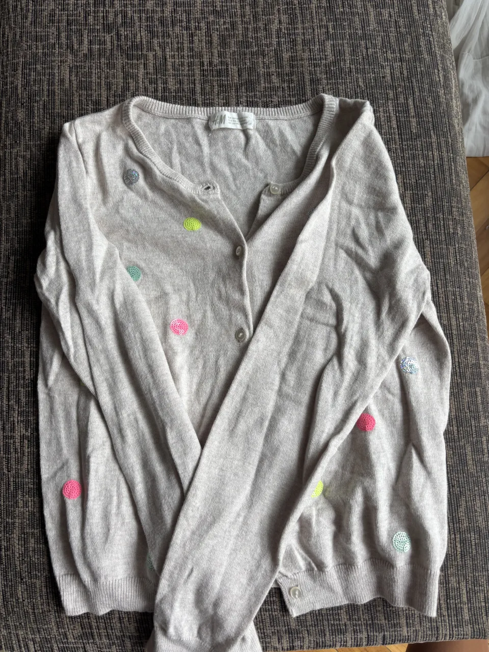 Cardigan de hilo color crudo con detalles de lunares de colores vibrantes (rosa, verde lima, celeste, plateado). Es un modelo abierto con botones al frente, ideal para sumar un toque divertido a cualquier outfit.