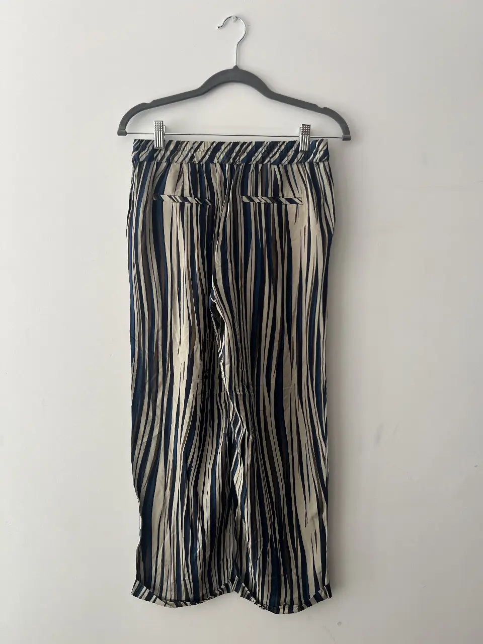 Pantalón sastrero de mujer con estampado de rayas verticales en tonos blanco, azul y marrón. Tiro medio, con bolsillos traseros y delanteros. Ideal para un look casual o de trabajo.