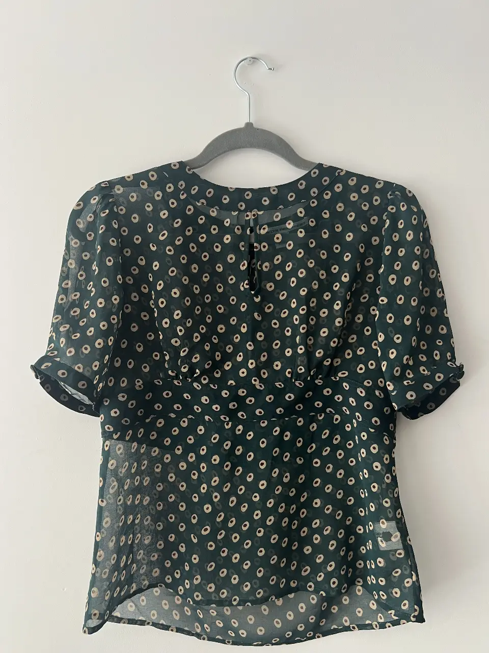 Blusa de mujer con estampado de lunares en verde oscuro y beige. Diseño con mangas cortas y detalle de botones en la parte trasera del cuello. Ideal para un look casual y elegante.