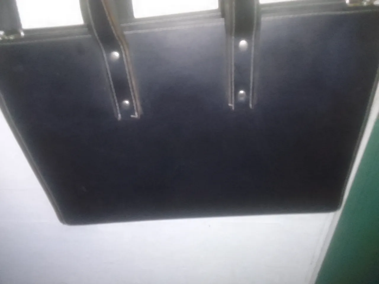 Cartera de mano negra, ideal para llevar documentos o una notebook pequeña. Cuenta con manijas y correa para colgar.