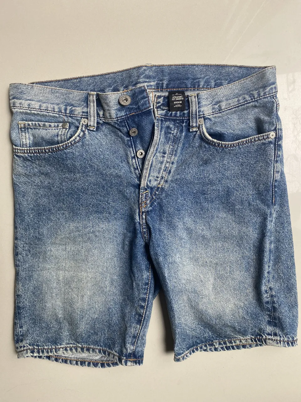 Shorts de jean, con lavado desgastado y roturas sutiles. Diseño clásico de cinco bolsillos y cierre de botones.