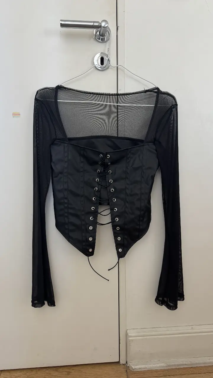 Top corset negro con mangas largas de red. Ideal para un look audaz y moderno.