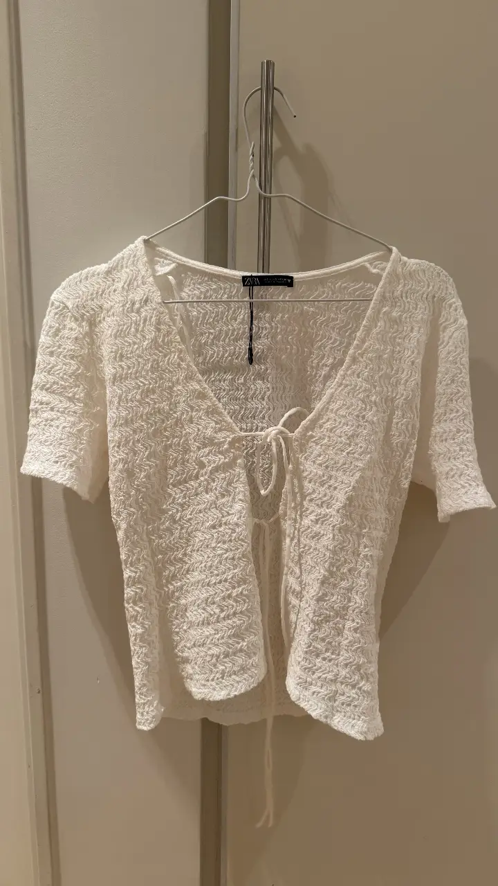 Blusa blanca de encaje con escote en V y lazo. Ideal para un look fresco y femenino.