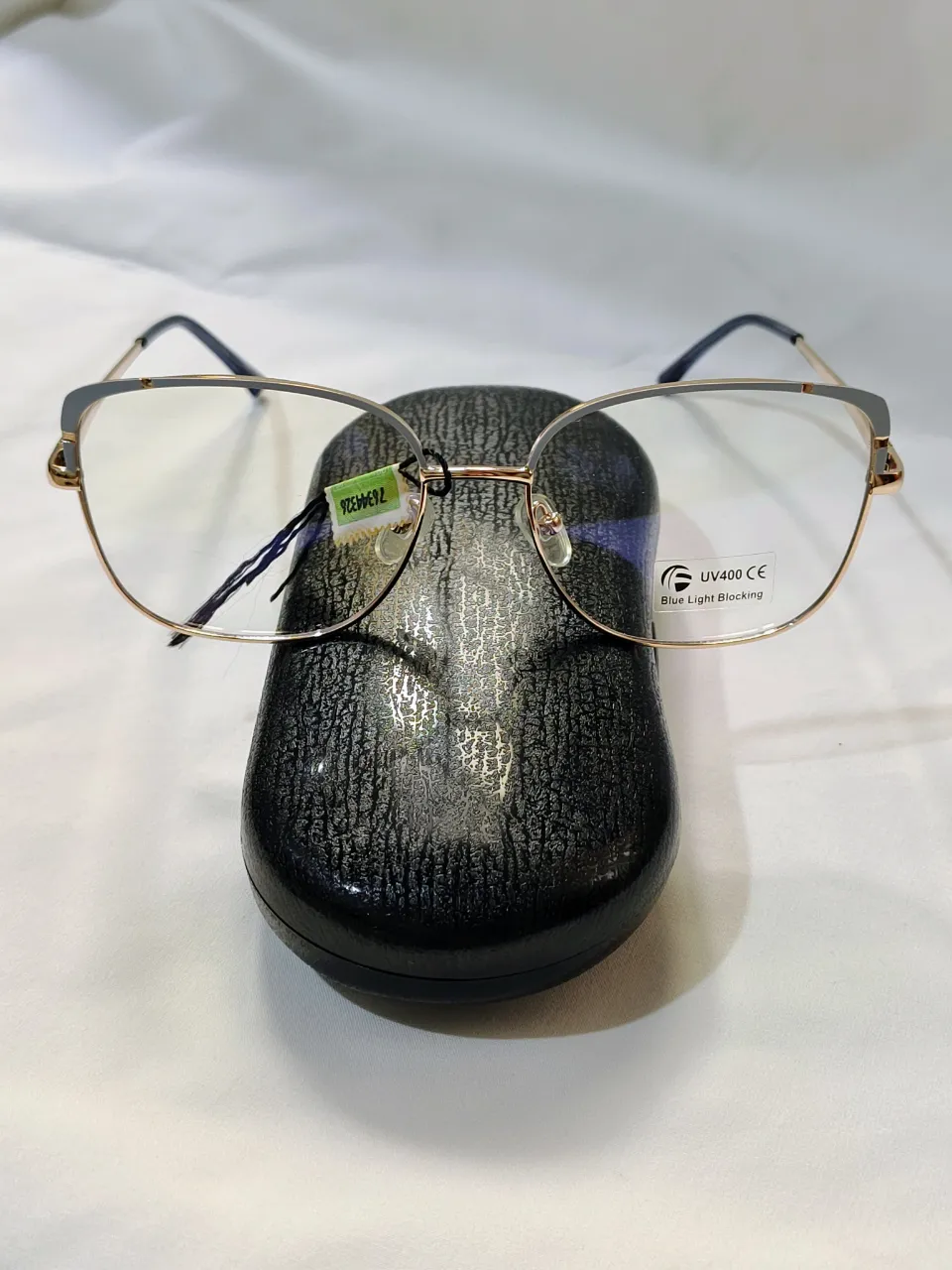 Anteojos con armazón metálico dorado y detalle esmaltado en gris en borde superior; montura completa. Patillas flex. Ancho de patilla a patilla 13 cm