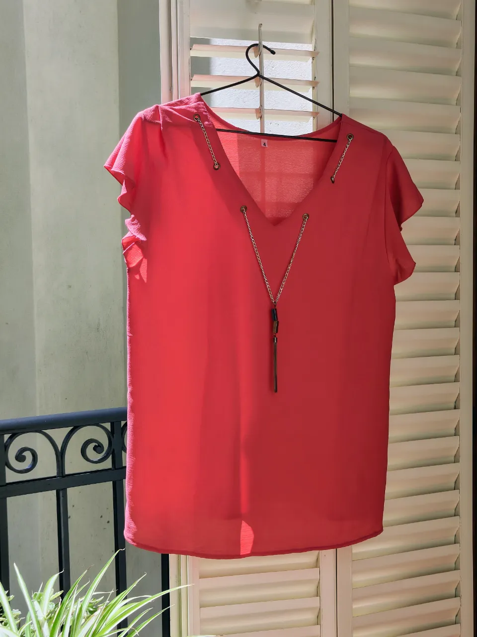 Remera manga corta de color coral Posee escote en V con detalle de cadenas plateadas y un colgante marrón en el centro. Las mangas son cortas y con volados. Ancho hombros 42 cm, ancho busto 51 CM, largo 67 cm