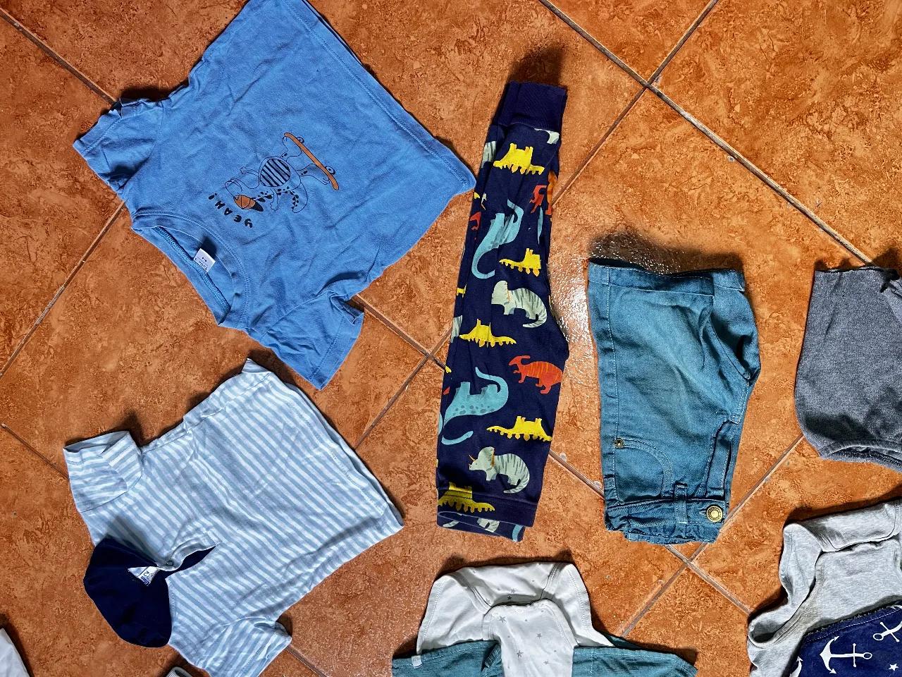 Conjunto de ropa de bebé con temática de dinosaurios y anclas. Incluye remera azul con estampa de dinosaurio, pantalón estampado de dinosaurios, remera a rayas, body gris con estampa de anclas, campera blanca con detalles de rayas y dos bodies/enteritos de algodón. Ideal para el día a día o para ocasiones informales. combo de 10 prendas. Para talle 1a2años mas o menos