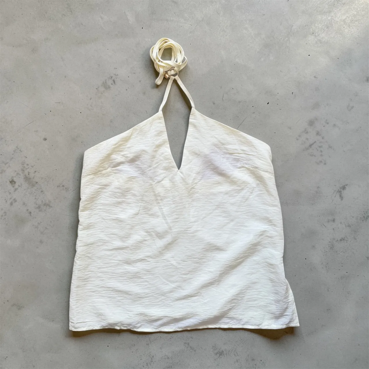 Top blanco con tiras finas que se anudan en el cuello. Escote en V pronunciado. Tela con textura.