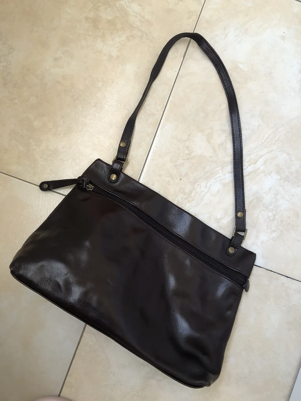 Cartera de cuero marrón oscura, con cierre principal y bolsillo exterior con cierre. Correa de hombro.