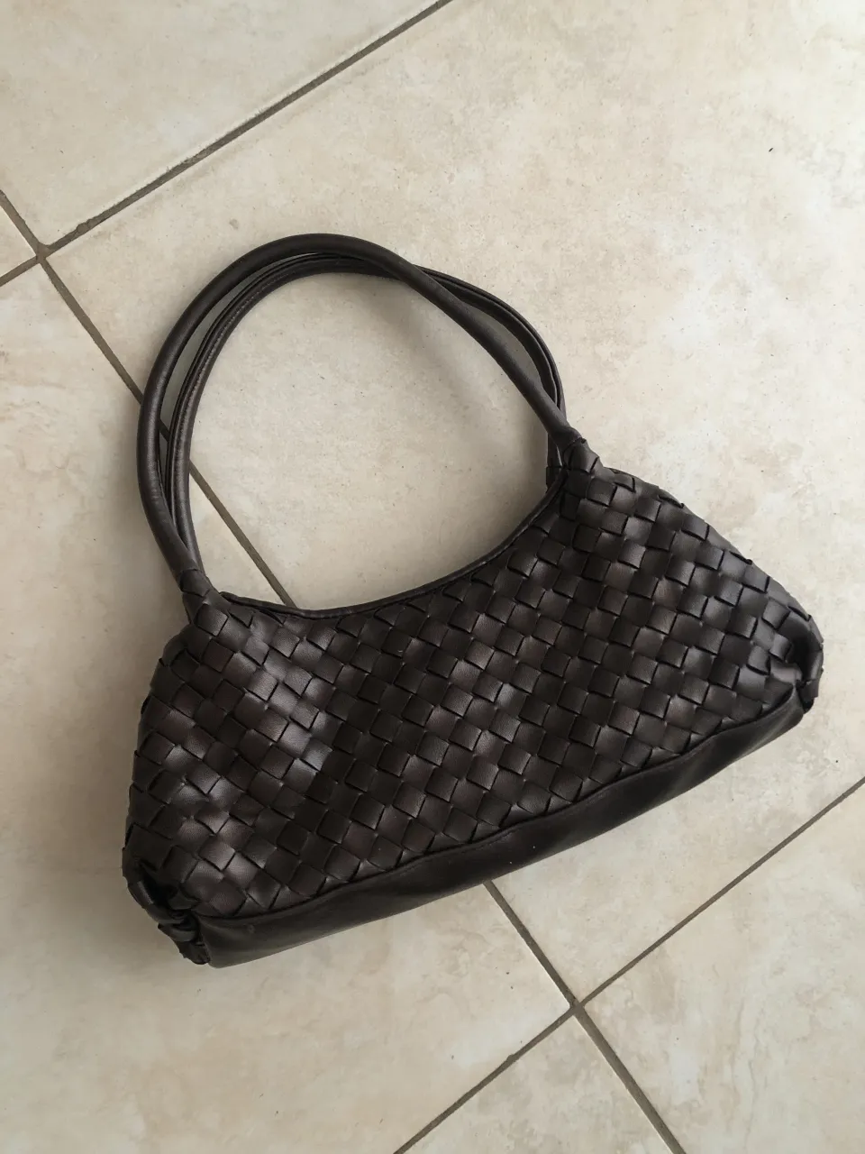 Bolso de eco cuero marrón tejido con detalle de flor en la parte frontal. Posee dos asas cortas y cierre principal. A pesar del tamaño es súper espaciosa 