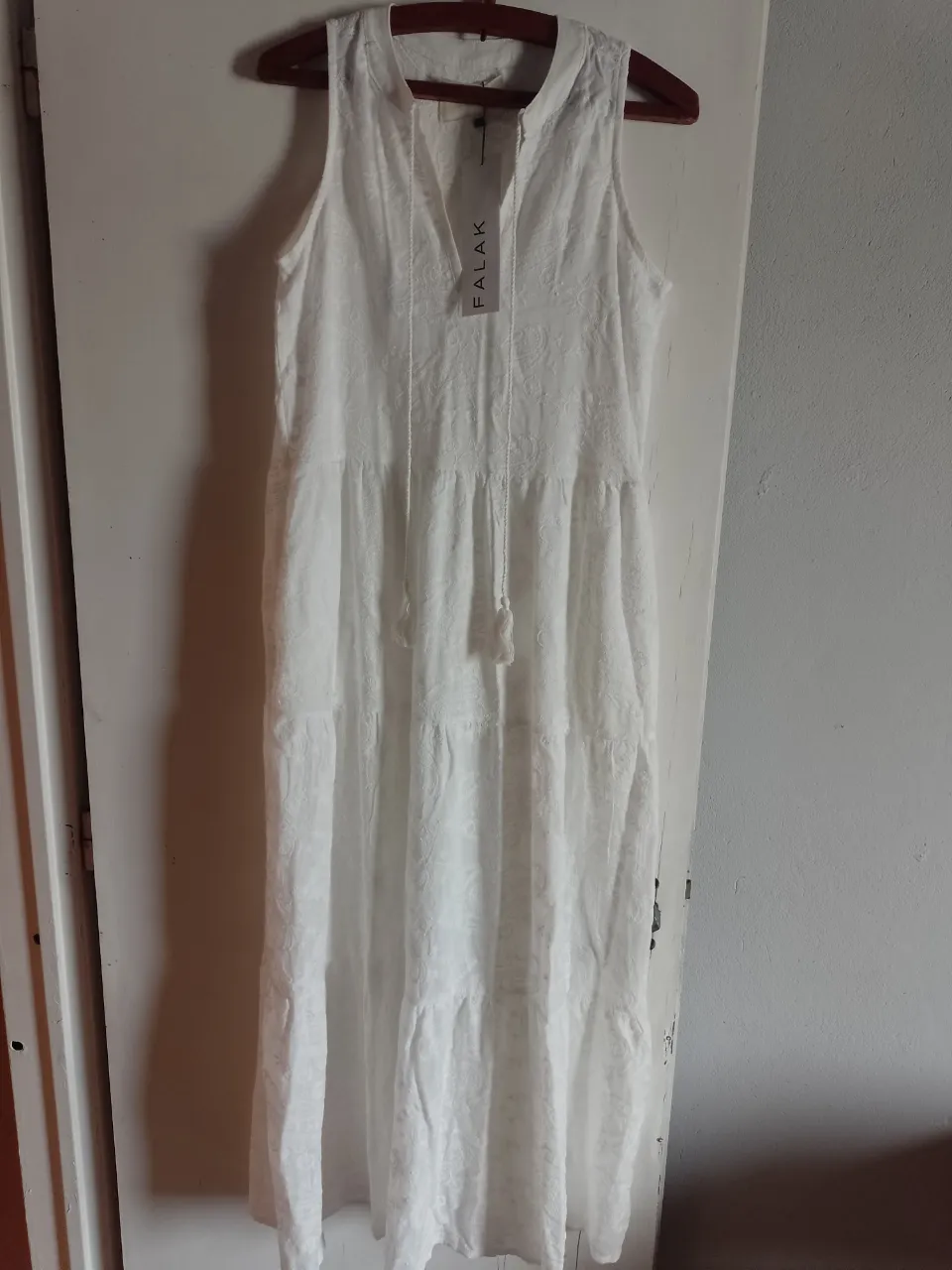 Vestido blanco largo, sin mangas, con escote en V y cordones. Posee un diseño sutil y delicado con detalles bordados y volados en la falda. Ideal para un look fresco y bohemio.