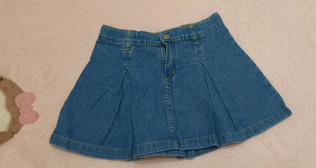 Pollera de jean azul con pespuntes a tono. Posee tabla en la parte delantera y trasera. Cierre y botón en la cintura.