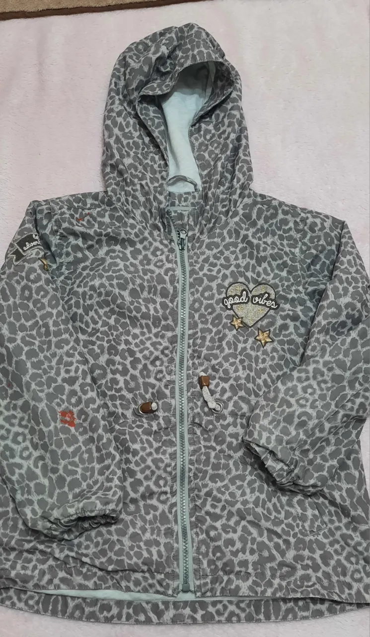 Campera con capucha y estampa de leopardo en tonos grises. Tiene cierre central, cordones ajustables en la cintura y parches decorativos en el frente.