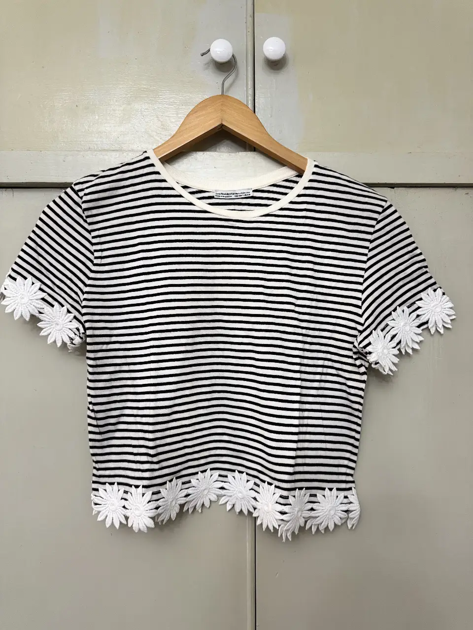 Remera crop de mujer a rayas horizontales en blanco y negro, con detalles de flores de encaje blanco en mangas y borde inferior. Ideal para un look casual y fresco. Marca Zara. 
