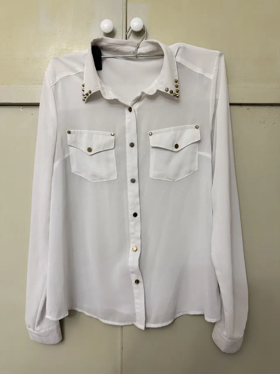 Blusa blanca con detalles dorados en el cuello y bolsillos. Ideal para un look elegante y sofisticado.
