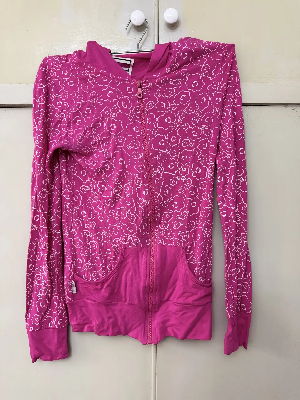 Buzo con cierre y capucha para mujer, de color rosa con estampado floral blanco. Ideal para un look casual y cómodo. Talle M ajustada al cuerpo, queda como S.