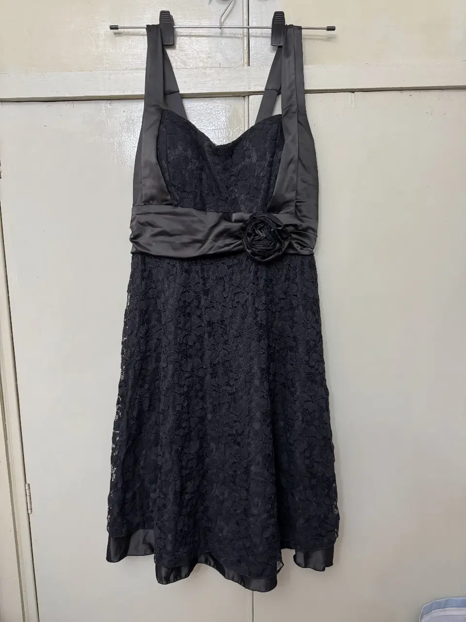 Vestido mini negro de encaje, ideal para eventos formales o fiestas. Diseño elegante con detalle de flor en la cintura y tirantes.