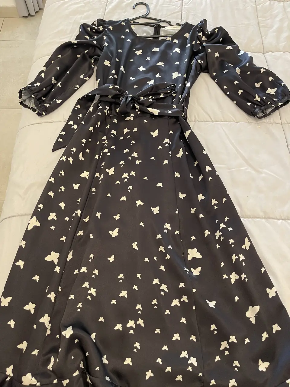 Vestido largo de mujer, negro con estampado de mariposas blancas. Con mangas largas abullonadas, cinturón para ajustar en la cintura y escote redondo. Ideal para eventos especiales o salidas.