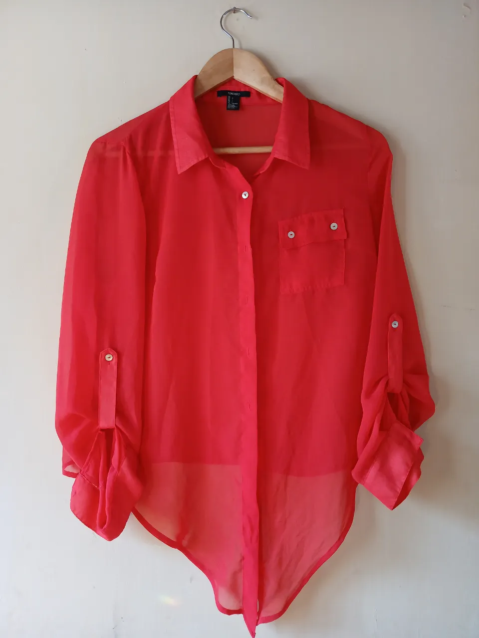 Blusa roja de Forever 21, de gasa, con mangas largas que se pueden arremangar con botón. Tiene un bolsillo en el pecho y un corte asimétrico en la parte inferior.
