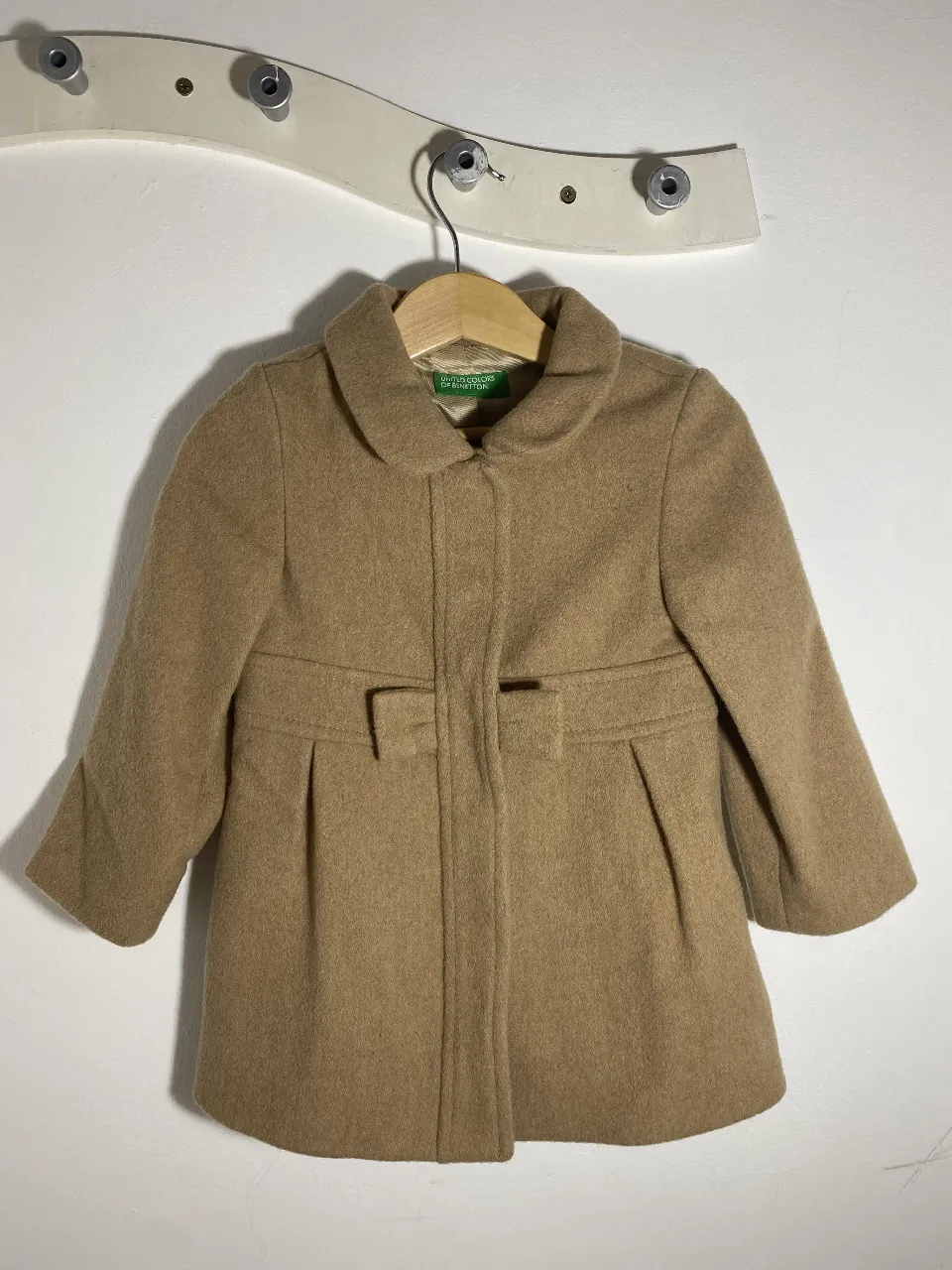 Abrigo de niña de la marca United Colors of Benetton, color marrón claro. Confeccionado en paño, este tapado presenta un diseño clásico con cuello redondo, cierre frontal con botones y un detalle de lazo en la cintura. Ideal para mantener a las pequeñas abrigadas y con estilo durante el invierno.