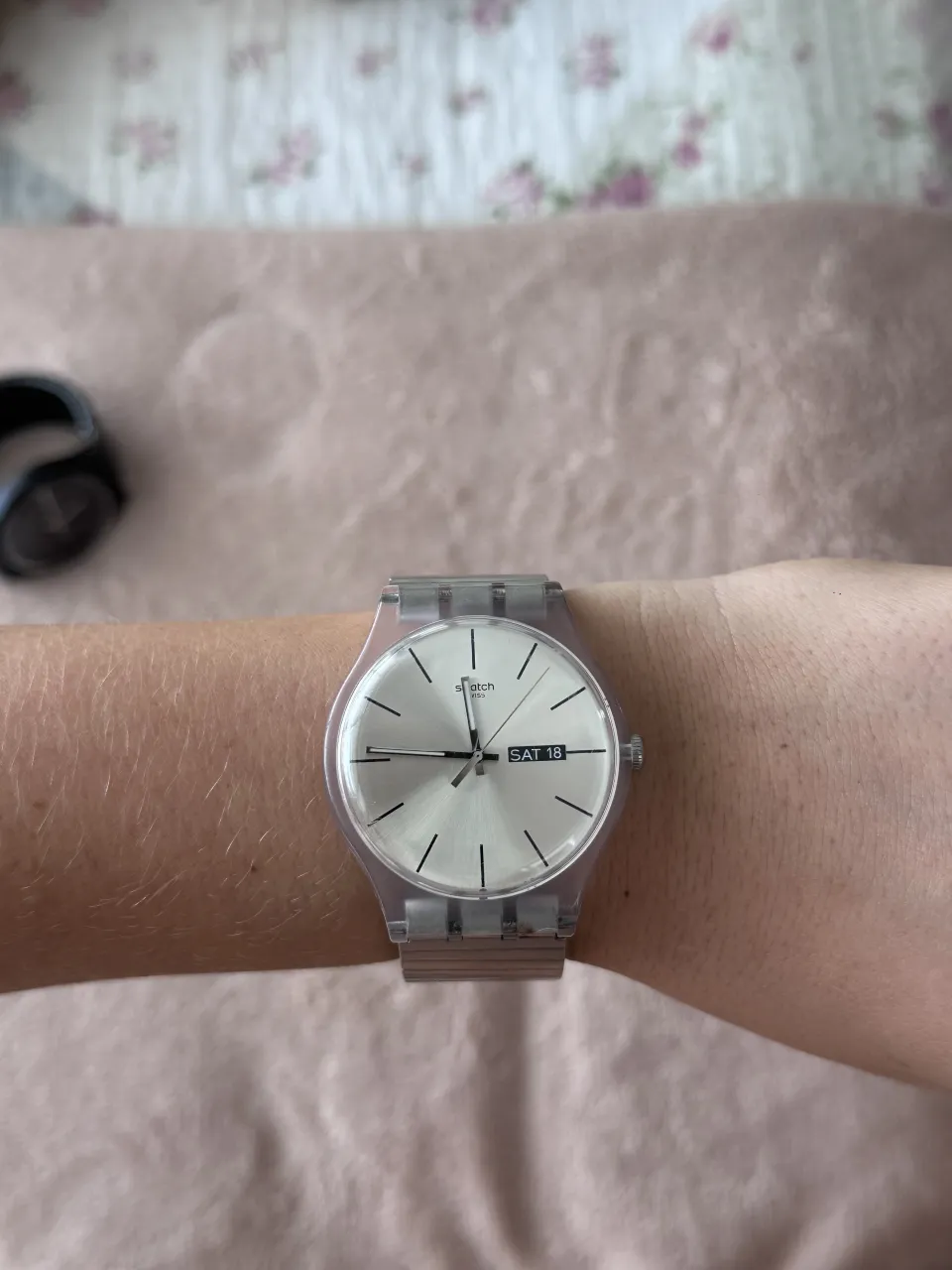 Reloj Swatch clásico con malla metálica extensible y caja transparente. La esfera es plateada con líneas finas y tiene indicador de día y fecha. Un modelo atemporal y versátil, perfecto para el día a día.