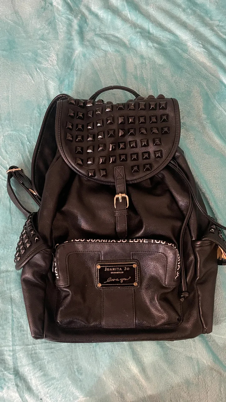 Mochila negra con tachas y detalles de la marca Juanita Jo. Todos los cierres y forro interno sanos. El cuero está minimamente razgado en un bolsillo por mi gato y en la parte de abajo (pero no se ve a no ser que lo busques) por el uso.