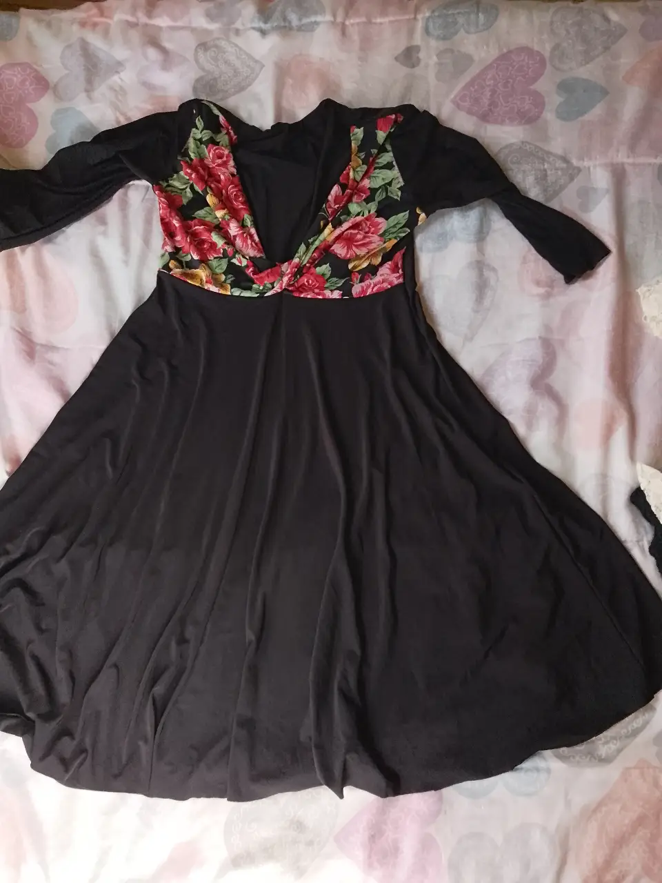 Vestido midi negro con escote en V y mangas largas. La parte superior del vestido presenta un diseño floral en tonos rojos y rosas, creando un contraste elegante. Ideal para eventos especiales o salidas nocturnas.