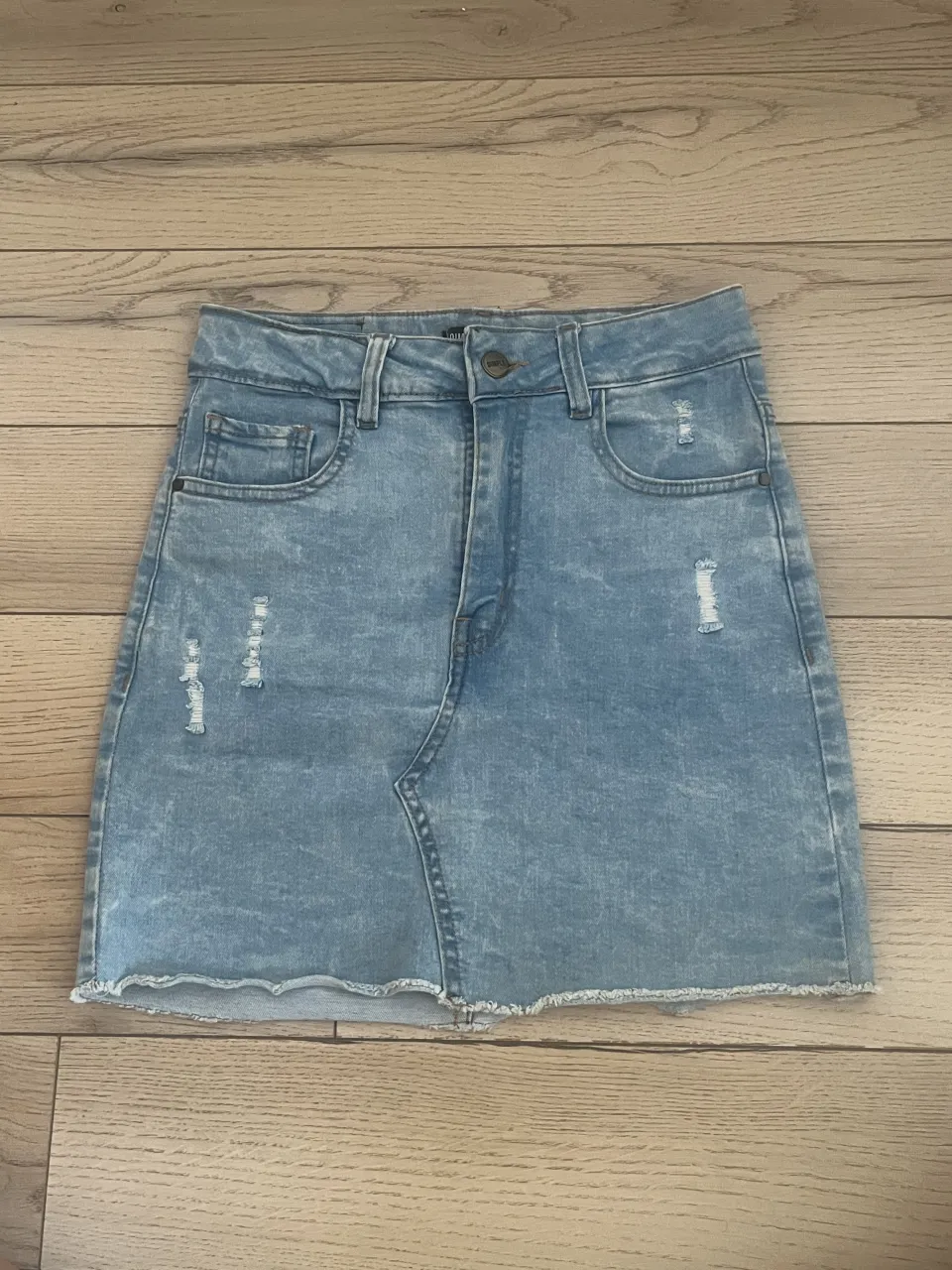 Pollera de jean tiro alto, con roturas y terminación deshilachada. Posee bolsillos delanteros y traseros.