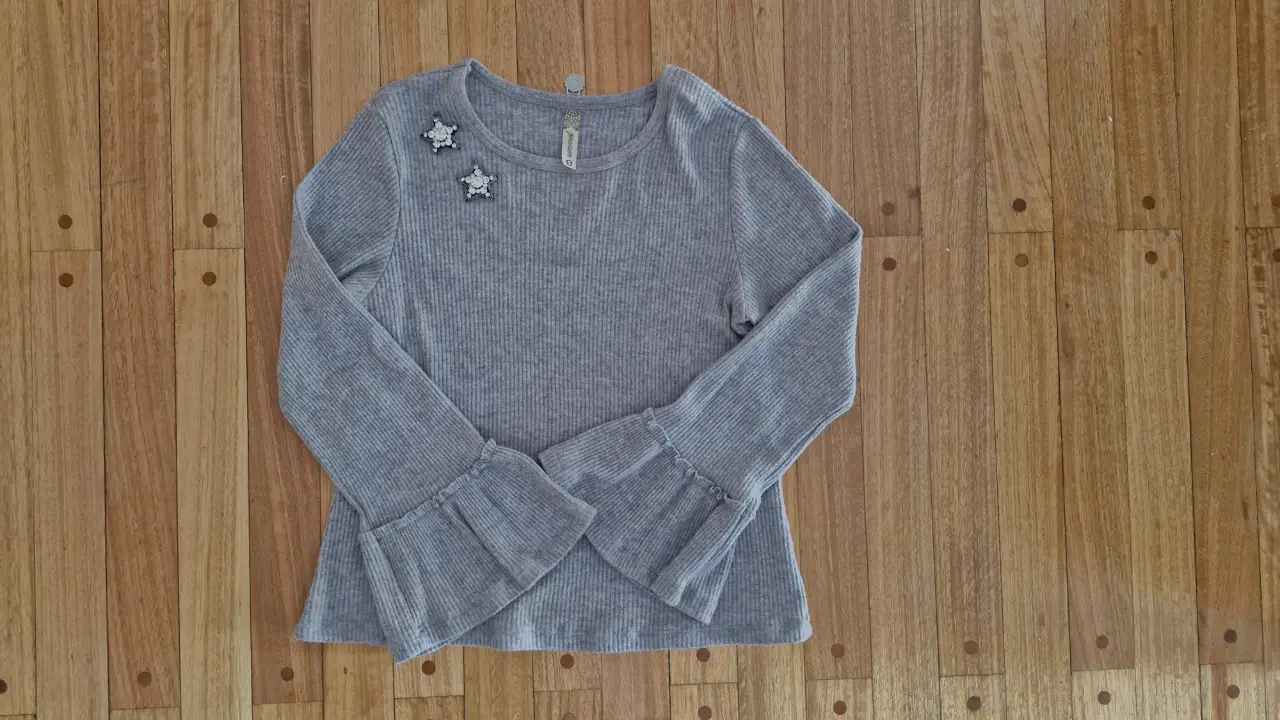 Remera de lanilla gris de manga larga con detalles de estrellas en los hombros y mangas acampanadas. 