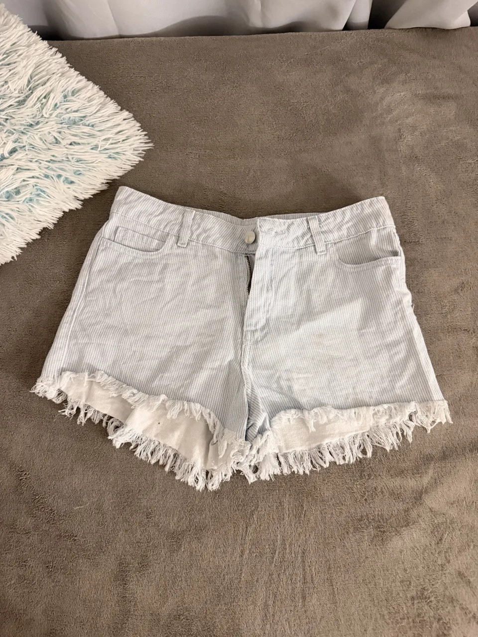 Shorts de jean tiro alto con rayas celestes y blancas. Tienen roturas y flecos en el borde inferior. Ideales para un look casual de verano.