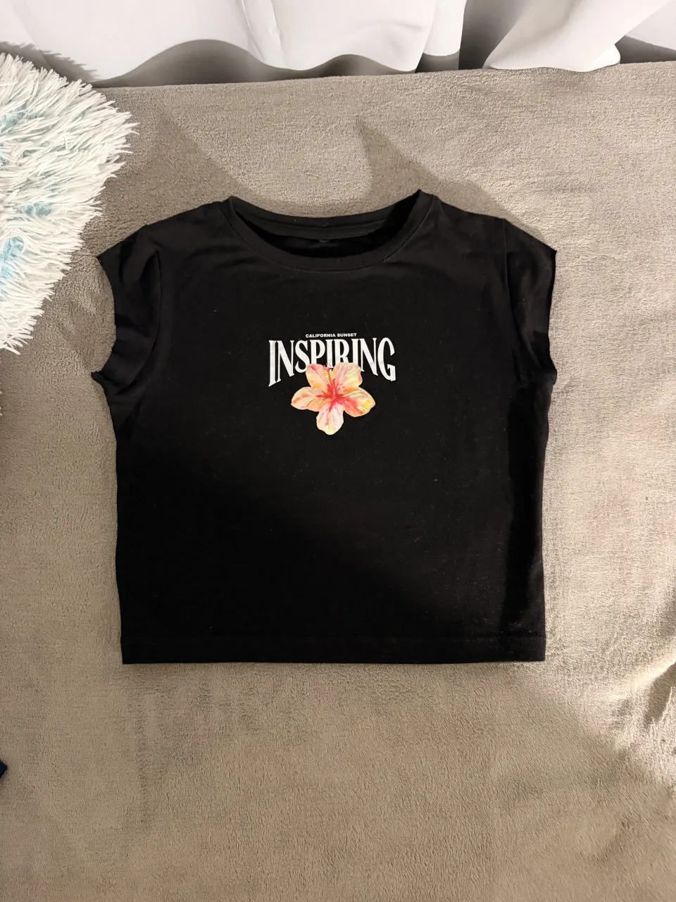 Remera negra crop con estampa "CALIFORNIA SUNSET INSPIRING" y una flor en el frente. Ideal para un look casual y moderno.