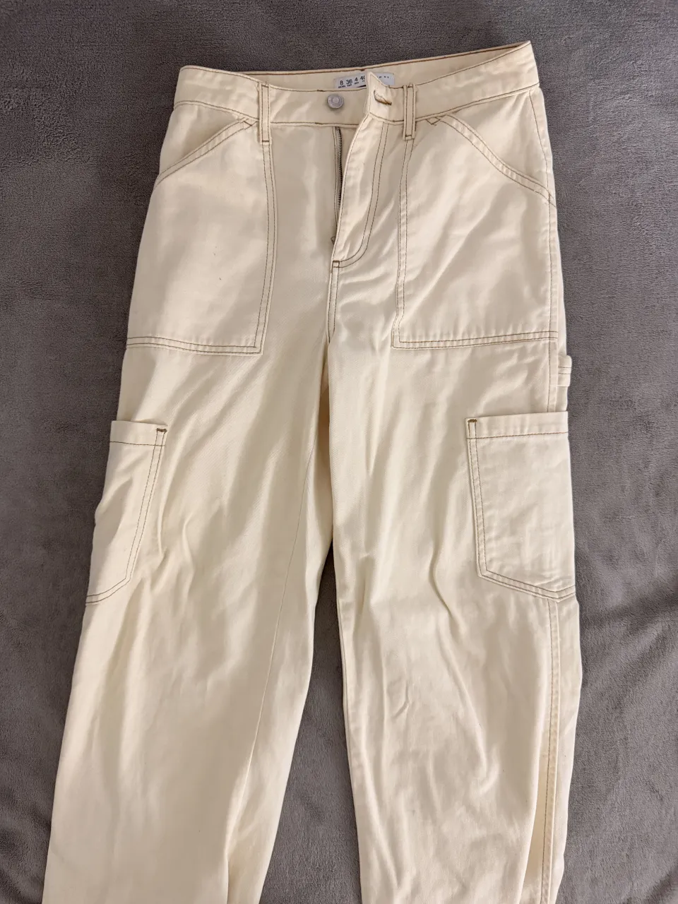 Pantalón cargo de gabardina color crudo, con bolsillos laterales y detalles de costura a la vista. Estilo urbano y moderno, ideal para el día a día.