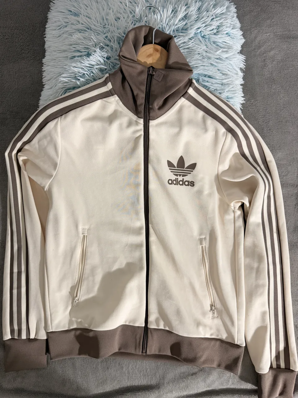 Campera deportiva Adidas original, color blanco tiza con detalles en marrón. Posee cierre completo al frente, cuello alto y puños elastizados. Ideal para un look casual y deportivo.