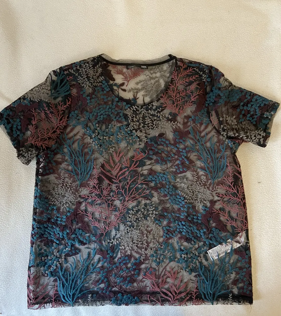 Blusa de encaje floral de la marca Zara, con mangas cortas y cuello redondo. Ideal para un look casual y elegante.