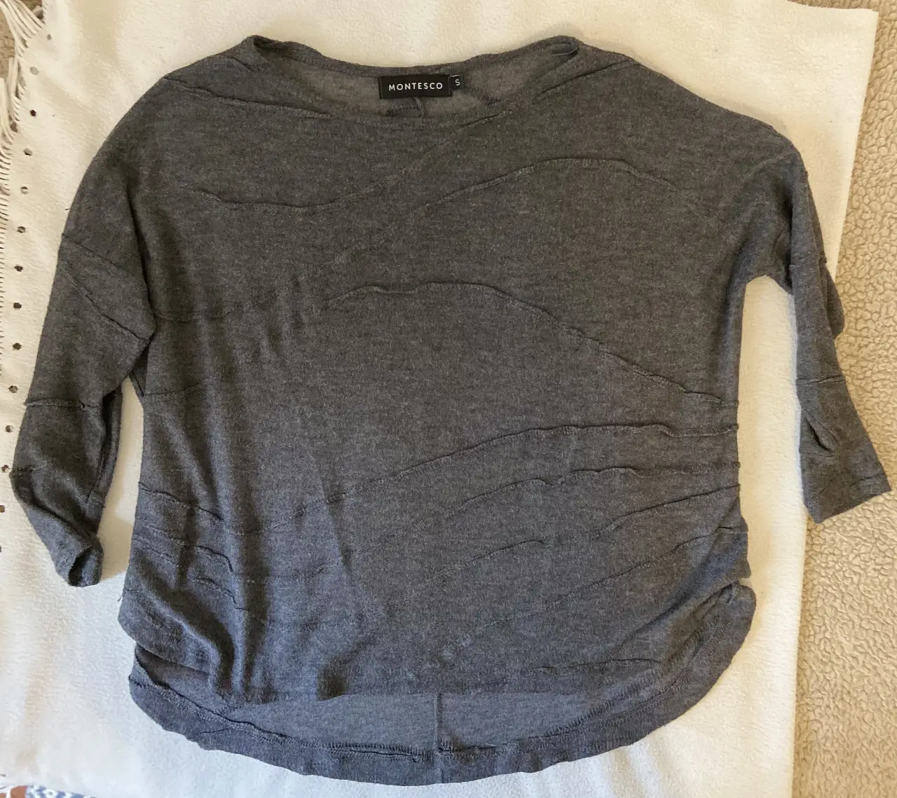 Sweater de mujer, color gris, con detalles ondulados en la parte delantera. Cuello redondo y mangas 3/4. Ideal para un look casual y cómodo.