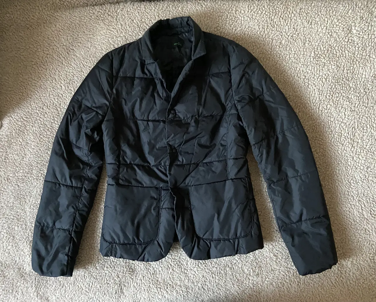 Chaqueta acolchada negra de la marca Benetton, con diseño tipo blazer. Posee dos bolsillos delanteros y cierre con botones. Ideal para un look casual y abrigado.