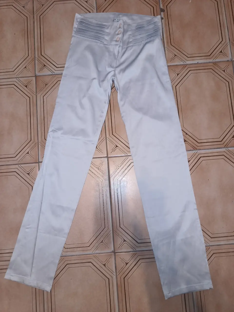 Pantalón sastrero de mujer, color gris claro, con detalles plisados en la cintura y botones decorativos. Ideal para un look elegante y sofisticado. Talle 1. impecable. Cintura:74cm Cadera:90cm Tiro del:24cm Largo:101 cm ancho de botamanga:17cm.