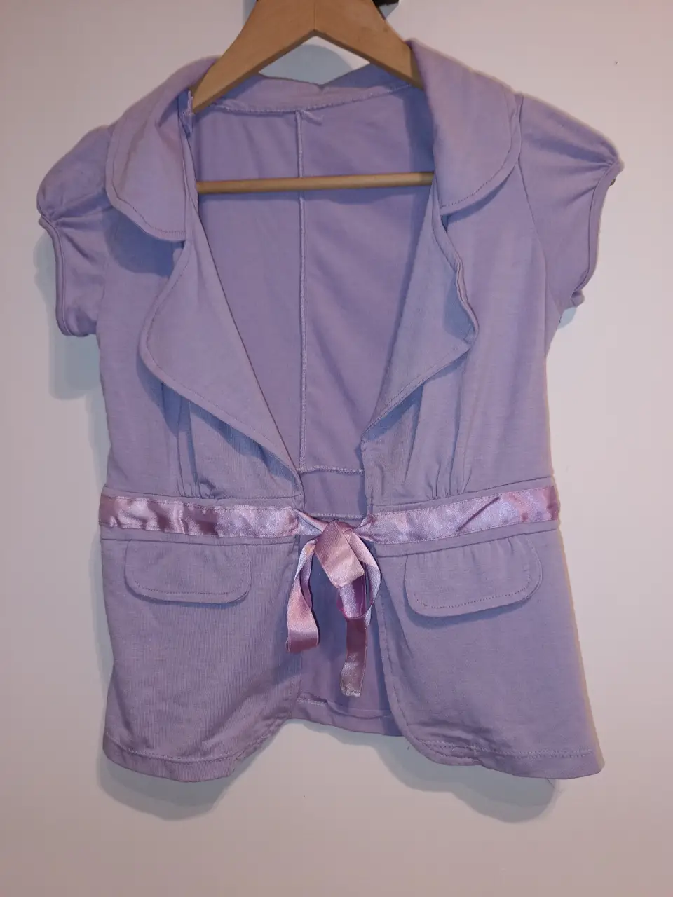 Saquito de manga corta en color lila con detalle de cinta rosa en la cintura y bolsillos simulados delanteros. Modal elastizado.Ideal para un look casual y femenino. Muy buen estado. entre hombros:38cm entre sisas:45 cm Largo:54cm