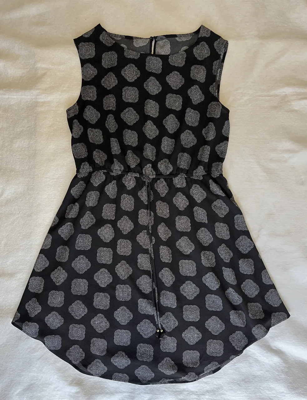 Vestido midi negro con estampado floral en blanco. Diseño sin mangas, con cintura entallada y detalle de lazo. Ideal para un look casual y fresco.