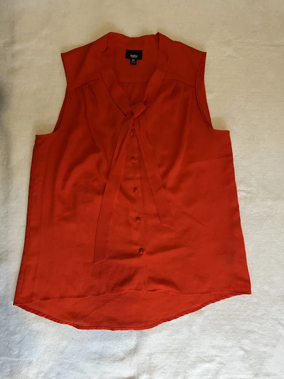 Blusa sin mangas de color naranja, con detalle de lazo en el frente y botones. Ideal para un look elegante y fresco.