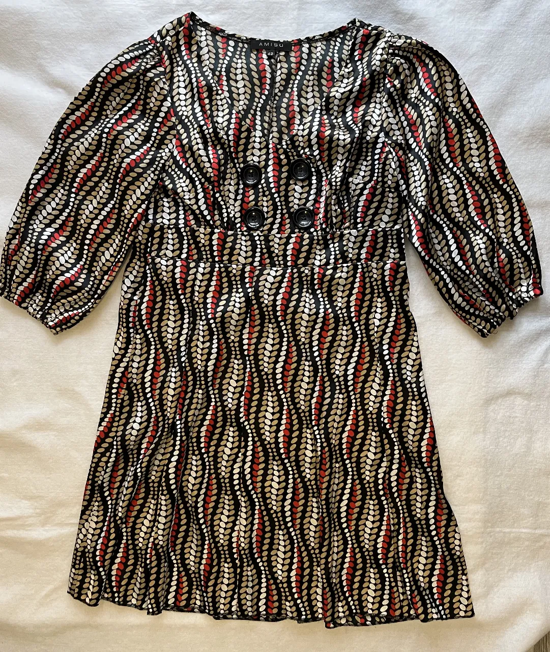 Vestido midi con estampado de diseño abstracto en tonos negro, rojo y beige. Corte a la cintura con botones decorativos y mangas 3/4 abullonadas. Ideal para un look elegante y con estilo.
