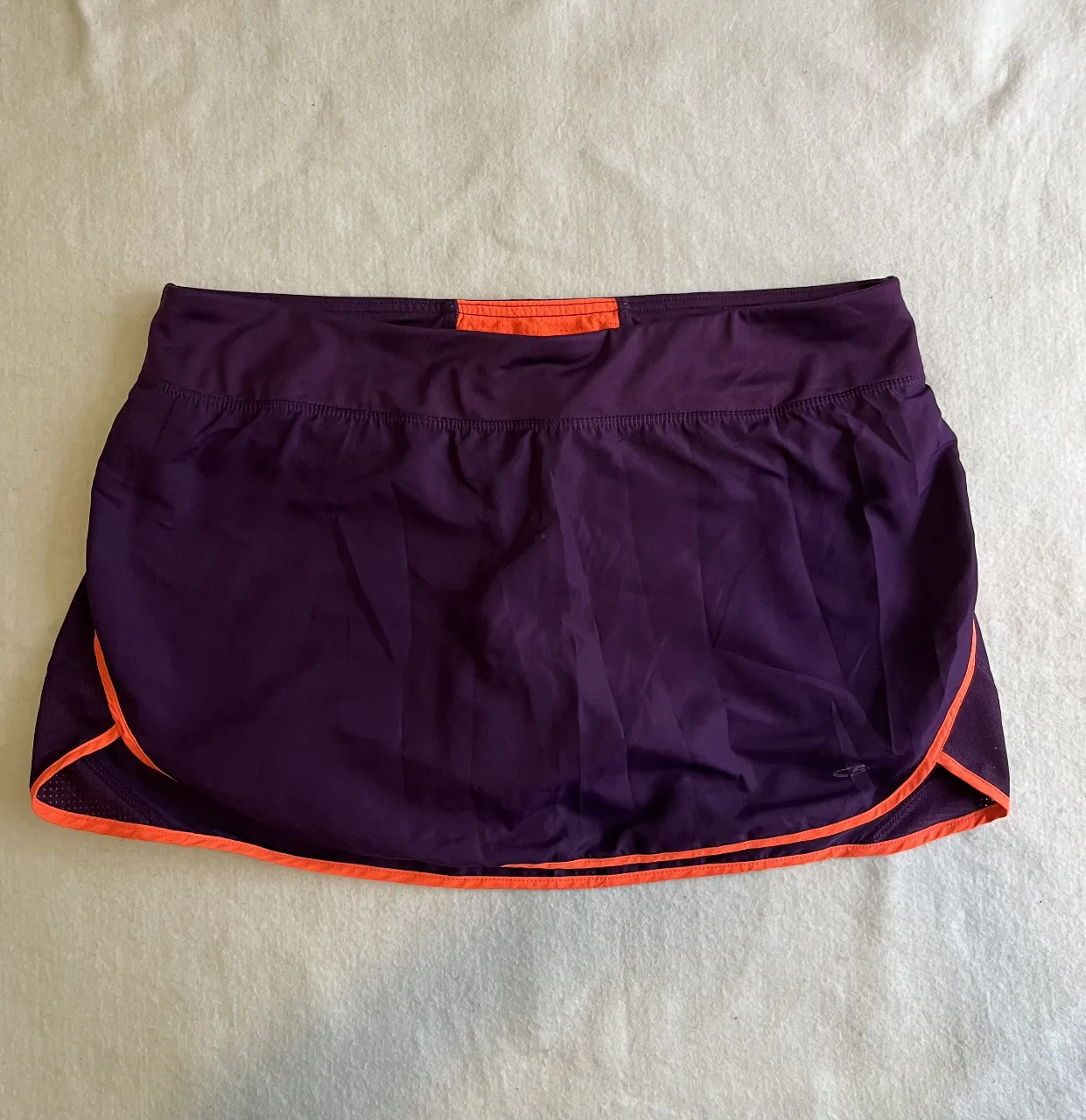 Short deportivo de mujer en color violeta con detalles en naranja. Ideal para running y actividades físicas.