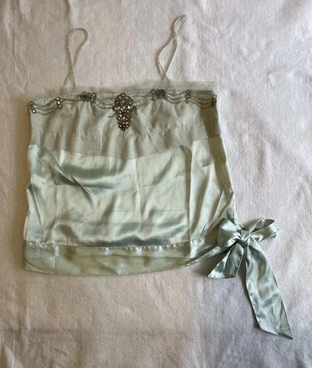 Top de seda celeste con detalles de pedrería y lazo lateral. Ideal para eventos especiales o para darle un toque elegante a tu look.