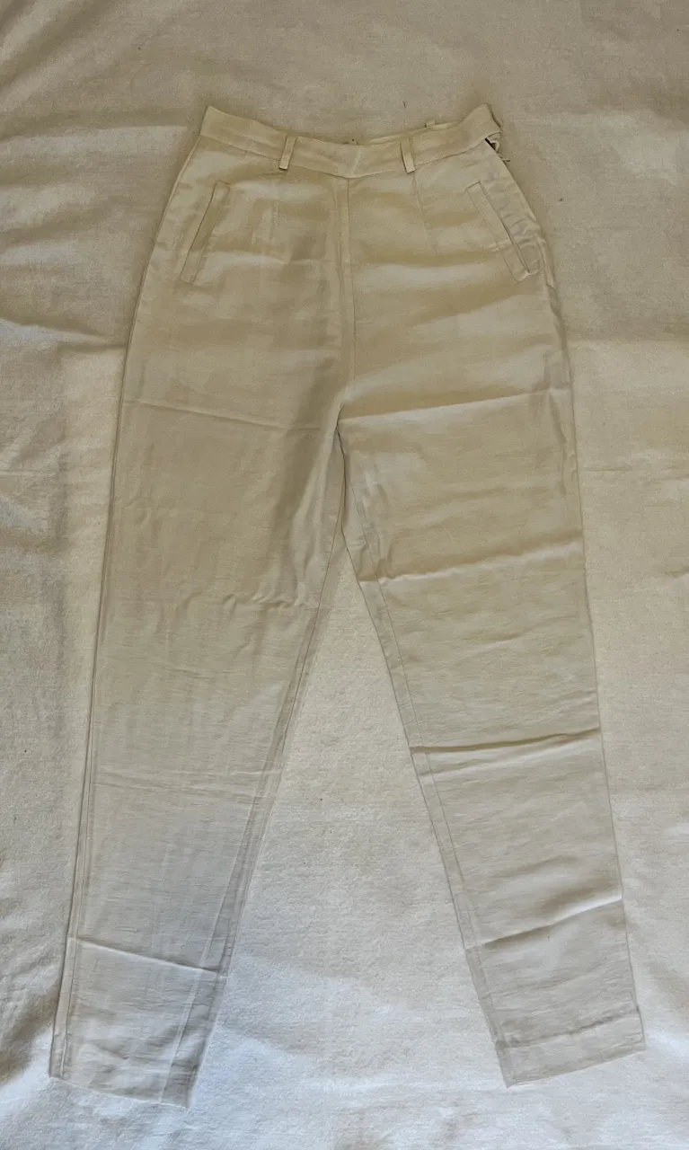 Pantalón sastrero de color crudo, tiro alto, con bolsillos delanteros y corte recto. Ideal para un look elegante y versátil.