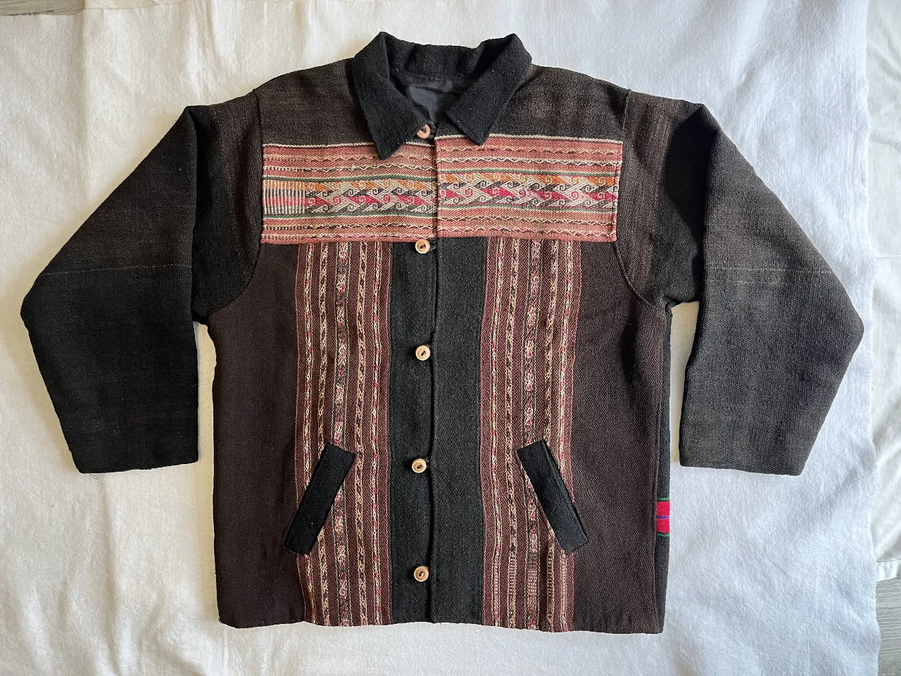 Campera artesanal oversize, con detalles en tela tejida en el frente y mangas negras. Posee botones de madera y bolsillos delanteros. Ideal para un look casual y abrigado.