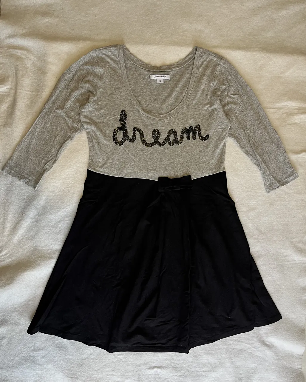 Vestido combinado gris y negro con detalle de lentejuelas "dream" en el frente. Posee mangas 3/4 y un moño en la cintura.