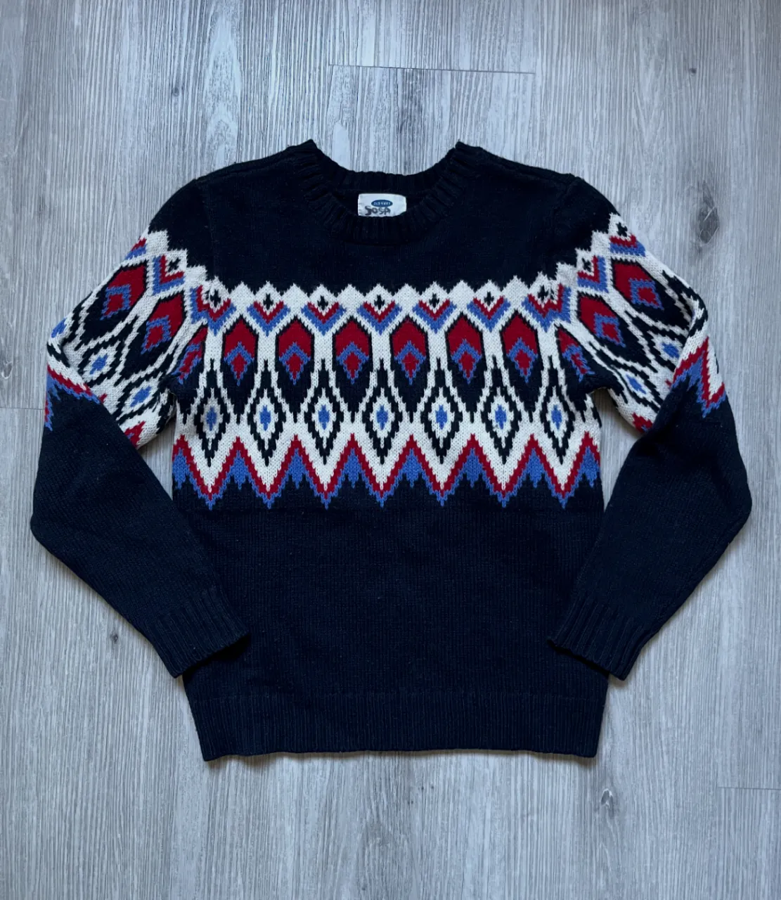 Sweater con diseño geométrico en tonos rojo, blanco y azul sobre fondo azul marino. Ideal para un look casual y abrigado.