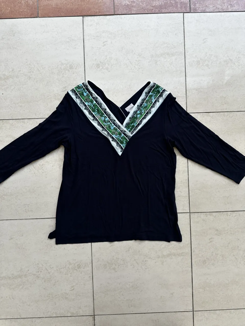 Remera negra de manga larga con escote en V adornado con un estampado floral y detalles de encaje blanco.